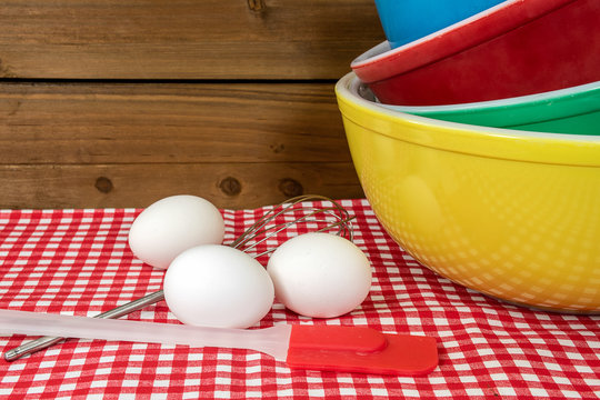 Stack Of Retro Mixing Bowls On Checkered Tablecloth With White Eggs And Kitchen Utensils