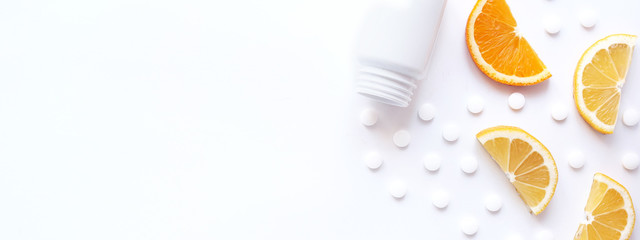 scattered vitamin pills and bottle with lemon orange on white background. Copyspace, flat lay, banner. Concept boost immune system, medicine and tablets.