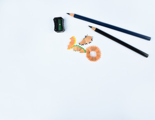Two black wood pencil,a black pencil sharpener and some pencil shavings