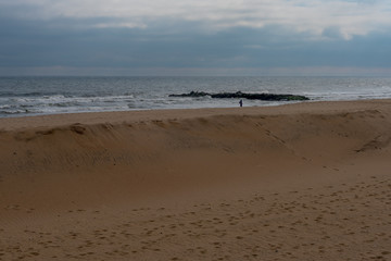 Fototapeta na wymiar Solo Figure Walking on Beach in Winter