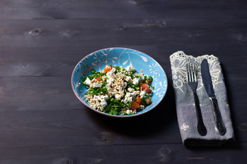 Blue plate of salad with green buckwheat, tomato, cottage cheese, parsley, pepper, olive oil, lemon  on black wooden background