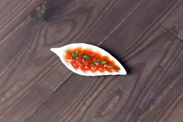 tomato sauce with scallions in leaf like bowl on brown wooden background