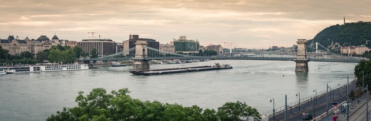 Naklejka premium Budapest Chain Bridge at dawn, panoramic view. A barge is passing on the Danube river, Hungary