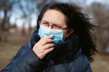 Prevention of coronavirus outbreak in 2020. Outdoor portrait of senior european woman wearing a disposable facial mask in city park or countryside. Prevent pollution and disease concept.