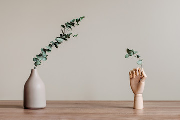 Dry eucalyptus branches in modern vase and wooden hand on the wooden table