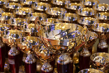 Fototapeta na wymiar beautiful gold cup on a background of cups for awarding. many beautiful gold cups for rewarding, gold cups for winners, collection of gilded goblets,championship award cups,award products for the comp