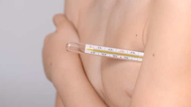 Mercury thermometer under the child's hand. Temperature measurement. Pandemic March 2020. The boy holds under his arm a means of measuring the temperature of the human body.