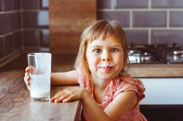 Happy little girl drinking milk or another dairy product from glass