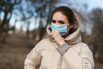 Prevention of coronavirus outbreak in 2020. Outdoor portrait of young european woman wearing a disposable facial mask. Prevent pollution and disease concept.