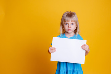 Fototapeta na wymiar маленькая девочка держит пустой лист бумаги на желтом фоне