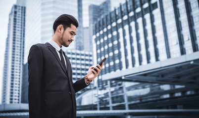 Young executive businessman using a mobile phone in the business district with skyscrapers buildings background	