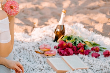 beautiful fair-haired girl sits on a plaid and holds a donut. Romantic breakfast at dawn, summer morning. photo session with a book and flowers tulips.