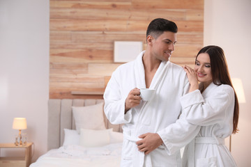Obraz na płótnie Canvas Happy couple in bathrobes with coffee in bedroom