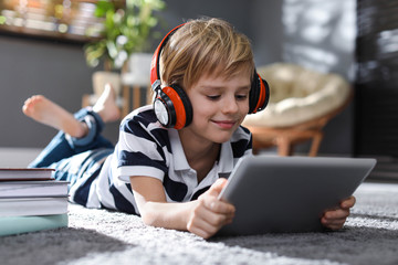 Cute little boy with headphones and tablet listening to audiobook at home
