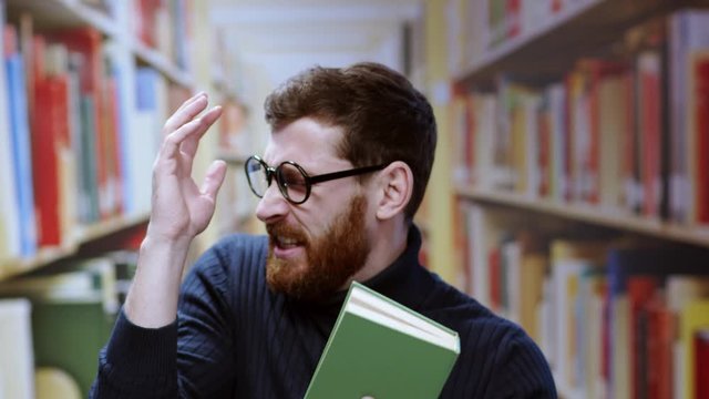 Displeased bearded man smelling bad smell getting furious shouting holding a book standing inside bookshelves at a library. Unpleasant situation. Comedy, fun concept.