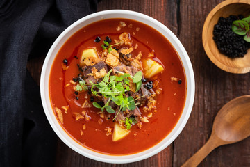 Tomato cream soup with smoked brisket and potatoes in a white bowl on a wooden background, top view and rustic style
