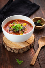 Tomato cream soup with smoked brisket and potatoes in a white bowl on a wooden background, rustic style