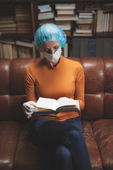 Woman with protective antiviral mask sitting at home in isolation / quarantine and reading book.
