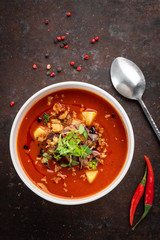 Italian tomato cream soup with meat, potatoes and green leaves in a white bowl on a rusty steel background