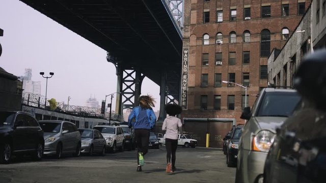 Joggers running outside in New York City with skyline and Brooklyn Bridge in background