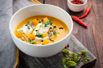 Bright colored pumpkin cream Soup with seeds and herbs in a white bowl on a wooden background, rustic style