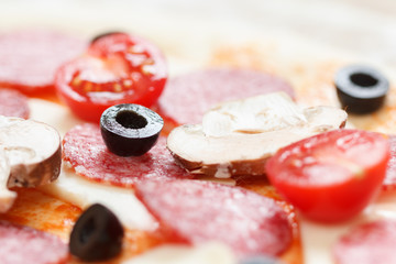 Raw pizza dough with olive over mozzarella, tomato and salami cooking
