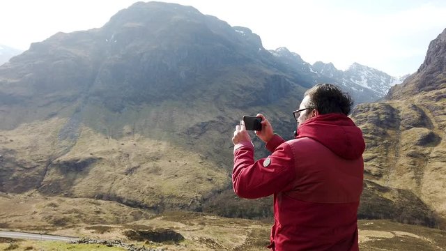 Man taking video of landscape Glencoe, Scotland, filming with a smartphone