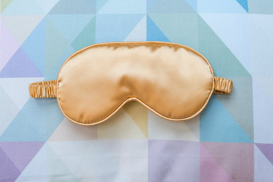 Golden sleeping eye mask on the bed, top view. Good night, flight and travel concept. Sweet dreams, siesta, insomnia, relaxation, tired, travel concept.Do not disturb, mask for sleep, bedtime concept