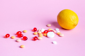 Lemon and scattered multi-colored pills on a pink background