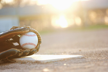 Baseball glove and ball on field during sunset with blurred background.