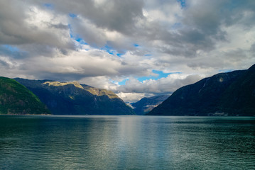 Cloudy sky over banks of fjord. Mountains with green forest, Eidfjord, Norway