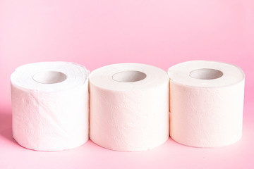 Three rolls of white toilet paper close-up on a pink background 
