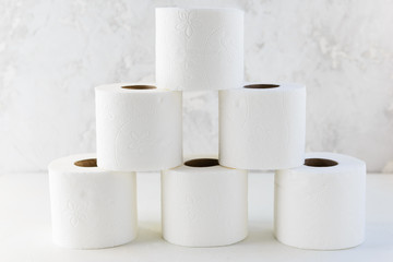 Rolls of white toilet paper in the form of a pyramid on a white table.