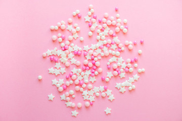 Colorful pastel sprinkles on a pink background. Sprinkle sugar with balls and stars, decoration for cake and bakery products.
