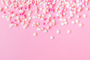 Festive frame made of colorful pastel sprinkles on a pink background, copy space on top. Sprinkle sugar with balls and stars, decoration for cake and bakery products.