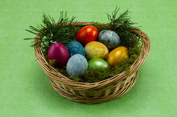 Easter, colored painted eggs in a wicker basket with moss and candle