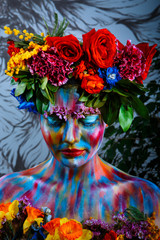 Portrait of a girl whose face is painted with colored paints in a wreath of flowers. In Frida Kahlo's footsteps