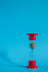 Red glass hourglass close-up against a blue background with copy space.
