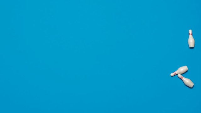 Stop motion animation of a bowling ball hitting bowling pins for a strike and knocking them all down on a blue backgroun.