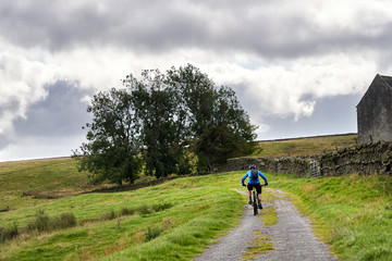 Obraz premium A cyclist riding a mountain bike up a dirst track for a cross country ride over remote English moorland, UK.