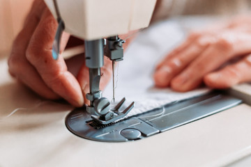 Womans hand sewing on the sewing mashine homemade medical mask.