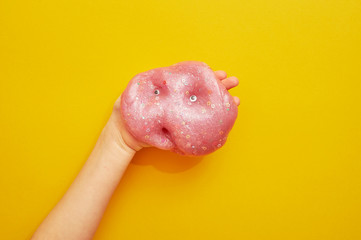 Pink slime with sequins on a yellow background, in a child's hand. With eyes. Creativity.