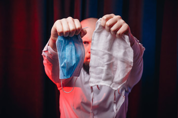 Frowned man holding gauze masks in hands on dark background. Emotion of anger and determination. Healthcare, respiratory illness prevention, prophylaxis of virus infections, COVID-19 concept.