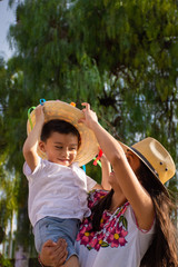 A Young Mexican mother carries her son wearing traditional mexican hats on the street