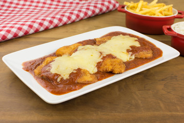 Veal parmigiana in a white platter with rice in and french fries in wood background