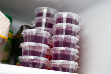 Obraz na płótnie Canvas A view of several condiment cups full of grape flavored gelatin shots, on display inside a home refrigerator.