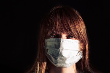 Close-up face of woman wearing a medical mask in studio on black background. Girl in medical mask against viruses and infections.