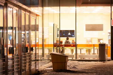 Small group of people in fast food restaurant on winter evening, seen from outside through window