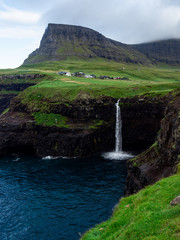 Faroe Islands, famouse Mulafossur Waterfall, its water falling into the ocean. Above there is a village Gasadalur.