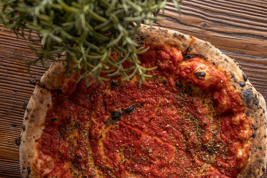 Zdjęcie pizzy Marinara, obok rozmaryn. Wszystko to na drewnianym, naturalnym, brązowym stole